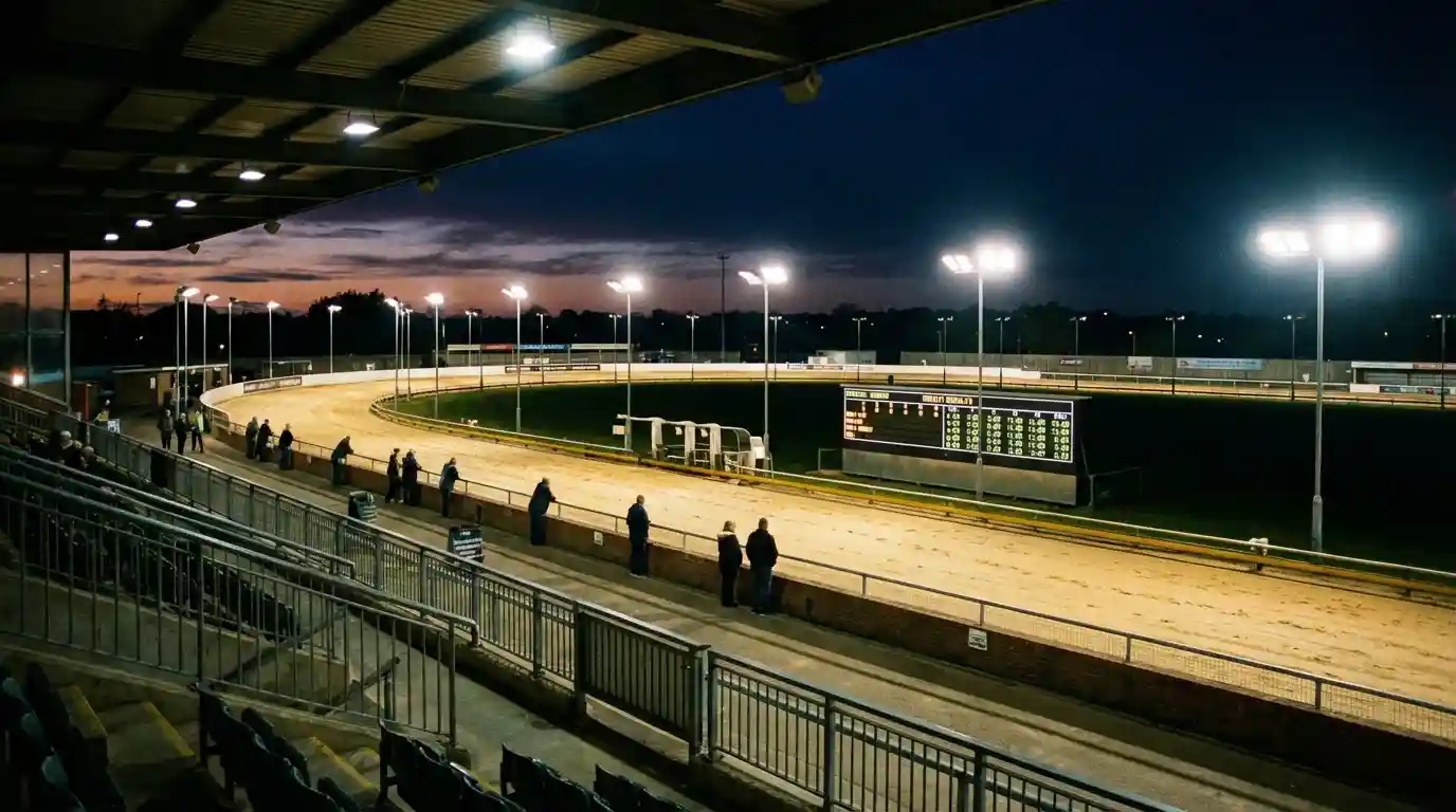 Aerial view of a UK greyhound track during evening racing with floodlit sand oval