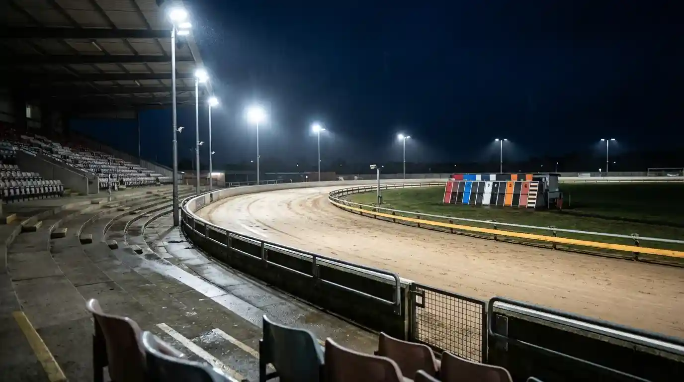 Floodlit UK greyhound racing stadium with sandy oval track seen from the grandstand at night